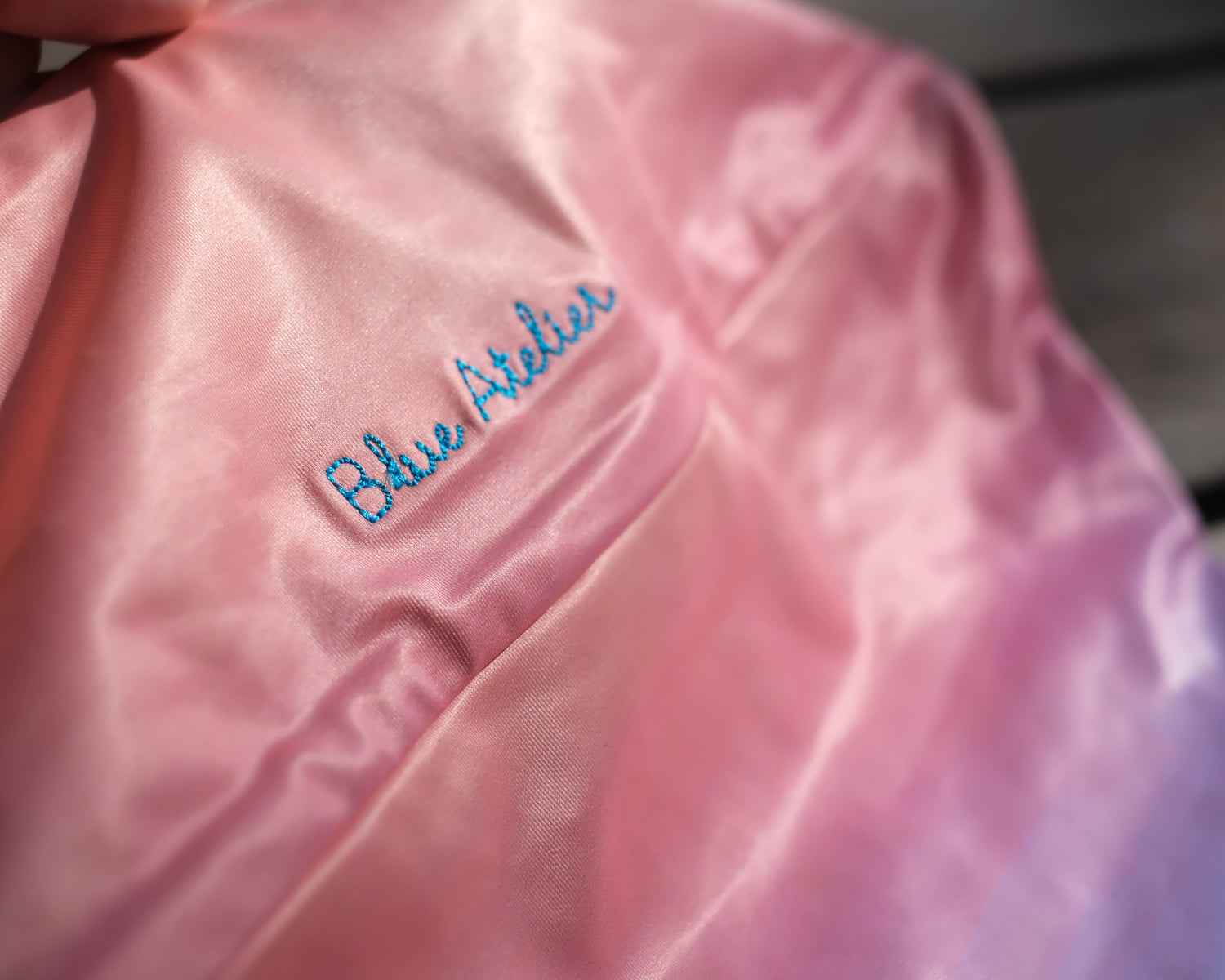 Close-up of a pink garment with 'Blue Atelier' embroidery.